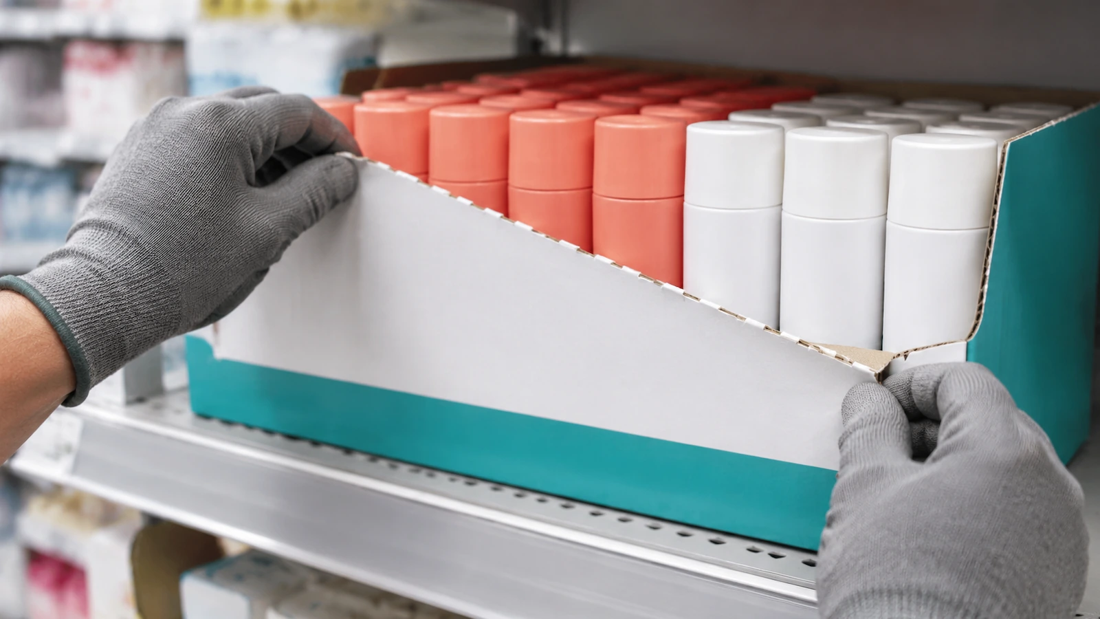 Dłonie zdejmujące perforowany przedni panel tacki gotowej na półkę z tektury falistej i odsłaniające równo ułożony produkt gotowy do wyłożenia na półkę